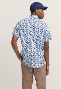 Kurzärmliges Hemd in Weiß mit blauen Blumenmustern. Verfügt über einen Kragen, einen lockeren Schnitt und einen abgerundeten Saum. Weicher Stoff mit subtiler Struktur.