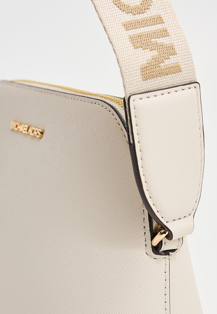 Bolso de mano de cuero sintético beige con herrajes dorados, que presenta una correa de tela desmontable con el nombre de la marca y un cierre cremallera.