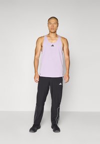 Lichtpaarse sporttanktop met zwart logo en donkere broek met witte accenten. Losse pasvorm en ademend materiaal, ontworpen voor beweging.