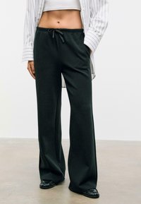 Zwarte wijde broek van zachte stof met een elastische tailleband en een trekkoord. Gepaard met een witgestreept shirt.