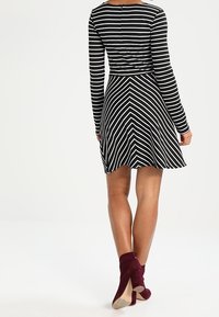Robe rayée noire et blanche à manches longues, présentant un corsage ajusté et une jupe évasée avec un motif en chevrons ; assortie à des bottines bordeaux.