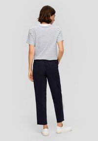 T-shirt rayé court en blanc et marine, associé à un pantalon cropped marine foncé. Modèle portant des baskets blanches, vu de dos.