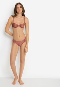 Μαγιό μπικίνι σε ροζ-χρυσό με δομημένο, ενισχυμένο τοπ και πλευρικές λεπτομέρειες. Ομαλή υφή, ρυθμιζόμενοι ιμάντες και ταυτόσημο χαμηλόμεσο κάτω μέρος.