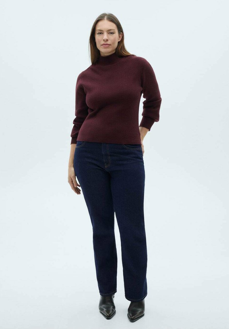 Burgundska rebraste turtleneck pulover v kombinaciji s temno modrimi straight-leg kavbojkami in črnimi škornji z ostrim nosom do gležnjev. Enobarvne barve, minimalno detajliranje.