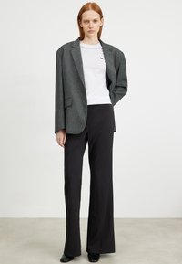 Grau strukturierter oversized Blazer über einem weißen T-Shirt, kombiniert mit schwarzen Schlaghosen und schwarzen Absätzen. Minimalistisches Design ohne Muster.