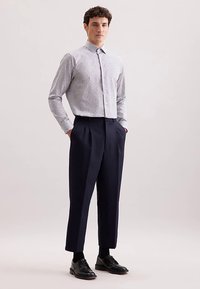 Lichtgrijs, patroon-knopenoverhemd met kraag, gecombineerd met hooggetailleerde, geplooide donkerblauwe broek en zwarte leren schoenen.