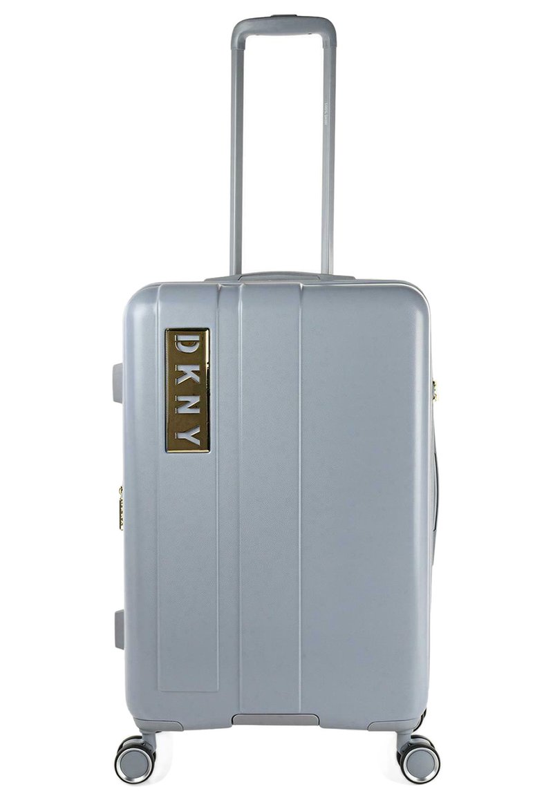 Maleta rígida plateada con surcos verticales, mango retráctil y cuatro ruedas. Logo de DKNY en dorado en la parte frontal.