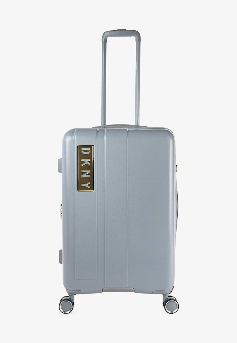 Maleta rígida plateada con surcos verticales, mango retráctil y cuatro ruedas. Logo de DKNY en dorado en la parte frontal.