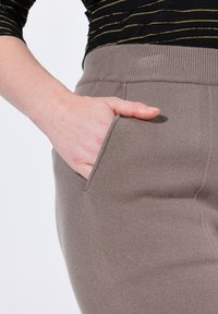 Dzianinowe spodnie w odcieniu taupe mają prążkowany pas i boczne kieszenie, prezentując miękką teksturę i wysmuklony krój.