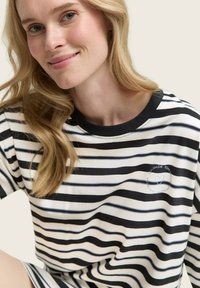 Gestreiftes T-Shirt in Schwarz und Weiß aus weichem Stoff, mit Rundhalsausschnitt und gesticktem Herz-Logo auf der linken Brust.