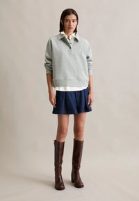 Light gray oversized sweatshirt, collared with three buttons. Paired with a white shirt underneath and a navy denim skirt. Brown knee-high boots.