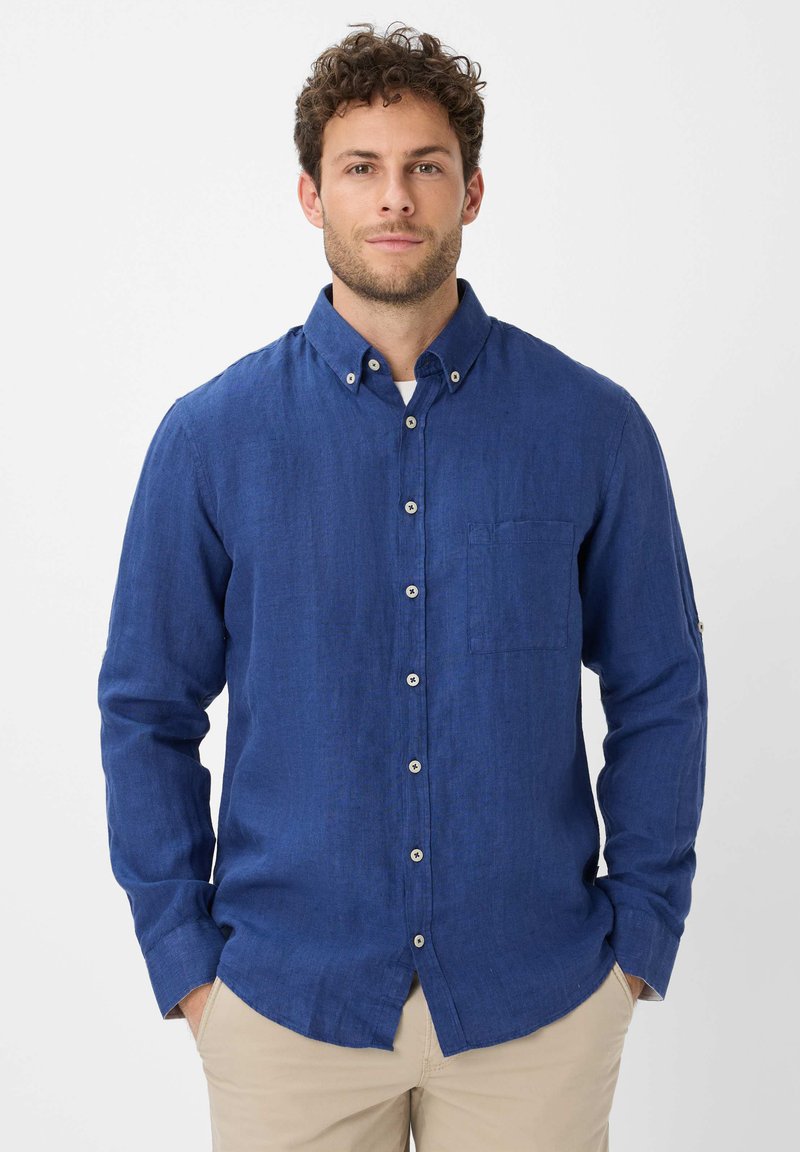 Camicia blu con bottoni, realizzata in tessuto leggero, dotata di taschino sul petto, colletto con bottoni e dettagli di cucitura visibili.