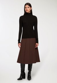 Czarny sweter w golf, brąskowa spódnica z plisami, czarne kozaki za kolano na słupkowym obcasie. Gładka tekstura z dopasowanymi i rozszerzającymi się elementami projektu.