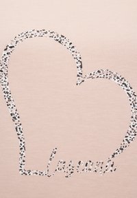 Hele roosa kangas, millel on suur südamekujuline kontuur musta ja valge laikudega mustris, sisaldab sõna "lasagna" juhuslikus kirjatüübis.