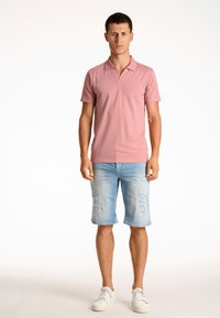 Rosa piketröja med krage, tillsammans med ljusblå slitna denimshorts och vita sneakers. En enkel, avslappnad design med mjukt tyg.
