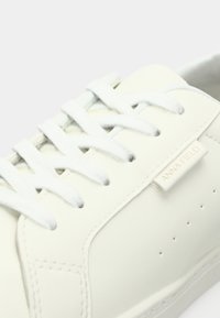Nahaufnahme eines weißen Sneakers mit weißen Schnürsenkeln und dem "ANNA FIELD"-Label an der Seite, das die Nähte und Perforationsdetails zeigt.