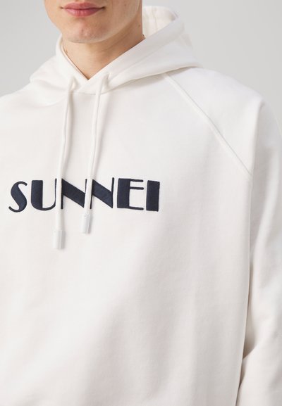 Hoodie bianco in cotone con logo "SUNNEI" ricamato in navy, dotato di cordini e maniche raglan. Texture liscia, design minimale.