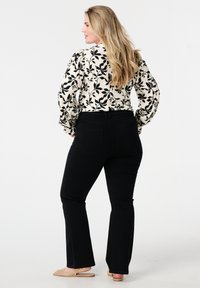 Zwarte flared jeans gecombineerd met een crèmekleurige blouse met een zwart bladpatroon. De blouse heeft pofmouwen en een gestructureerde stof.