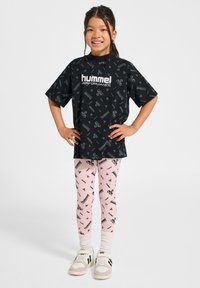 Svart t-shirt med Hummel-logotyp och mönster; rosa leggings med svart grafiskt tryck; vita strumpor och grå skor med svarta accenter.
