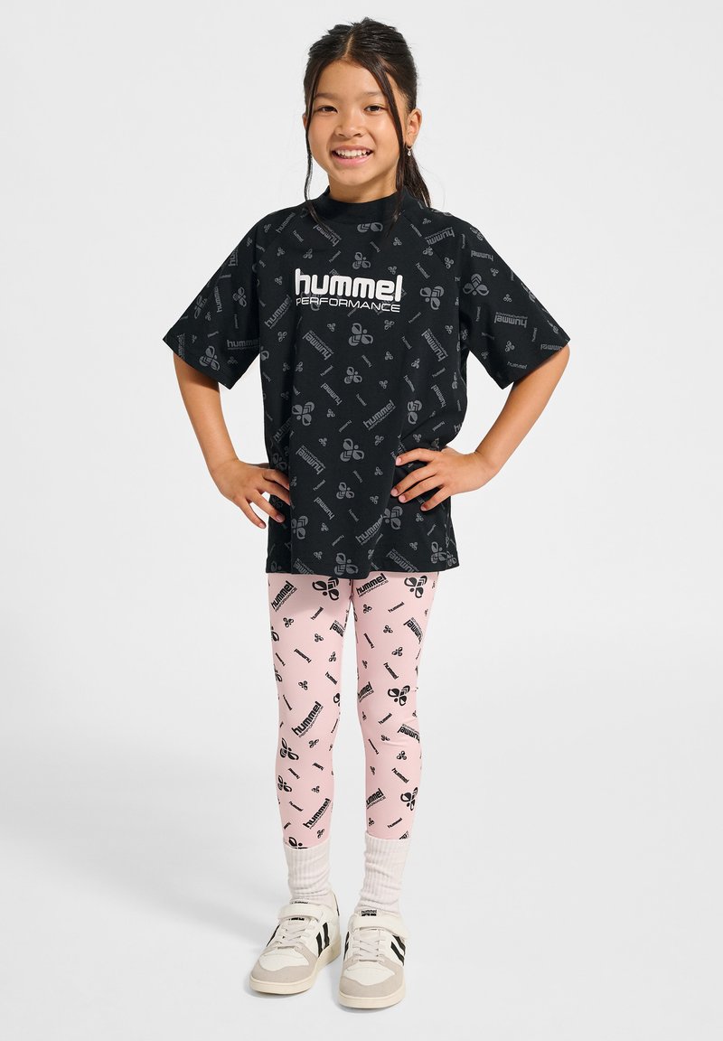 Svart t-shirt med Hummel-logotyp och mönster; rosa leggings med svart grafiskt tryck; vita strumpor och grå skor med svarta accenter.