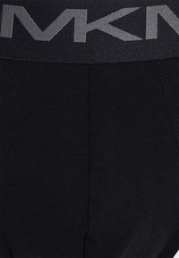Schwarze Leggings aus einem strukturierten Material mit einem breiten grauen elastischen Bund, auf dem das "MK"-Logo deutlich angezeigt wird.