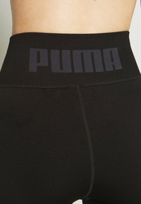Zwarte sportleggingen met een geribde tailleband, voorzien van een donker PUMA-logo, platgestikte naden en een gladde, rekbare stofstructuur.