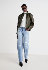 Chaqueta de cuero de moto verde oliva con cuello alzado, combinada con jeans rectos desgastados de color azul claro y tacones negros de punta.