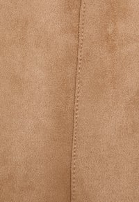 Primer plano de una tela de gamuza color beige que muestra una textura suave y una costura vertical en el centro.