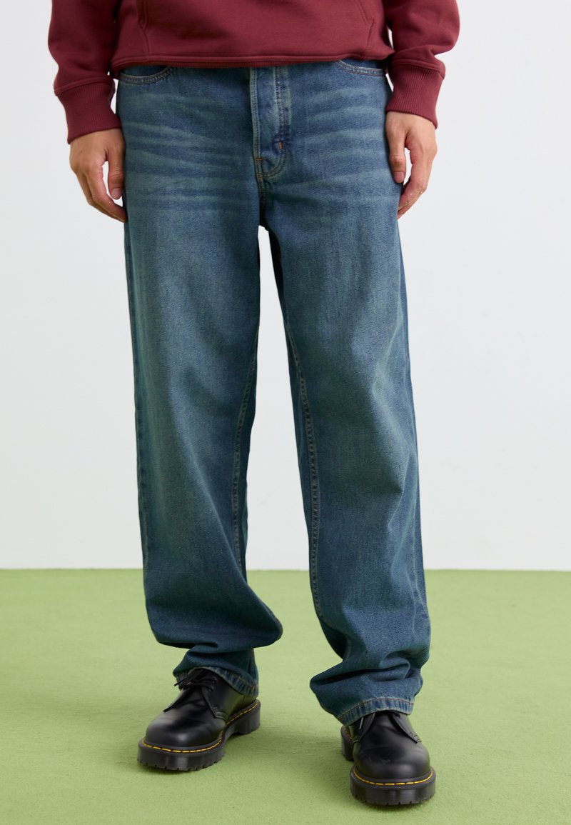 Relaxed-fit blue denim jeans with subtle fading, five-pocket design, and a straight leg. Paired with black platform shoes.