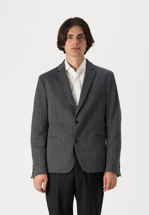 Grau gemusterter Blazer mit taillierter Passform, einreihiger Knopfverschluss, Reverskragen und zwei aufgesetzten Taschen, über einem weißen Hemd getragen.