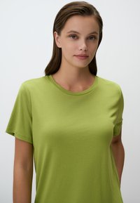 T-shirt a maniche corte, con collo giro in cotone verde brillante. Tessuto liscio e vestibilità comoda, con un design semplice e privo di decorazioni.