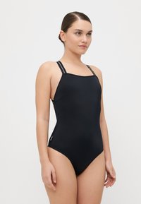 Črn enodelni kopalni kostim z tankimi, nastavljivimi naramnicami, kvadratnim izrezom in stranskimi izrezi. Gladek, raztegljiv material brez vzorcev.