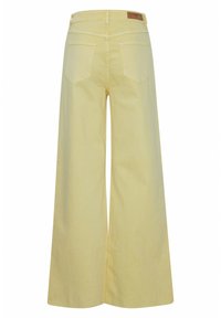 Pantaloni in cotone giallo a gamba larga con una texture liscia. Presentano due tasche posteriori e un'etichetta in pelle in vita.