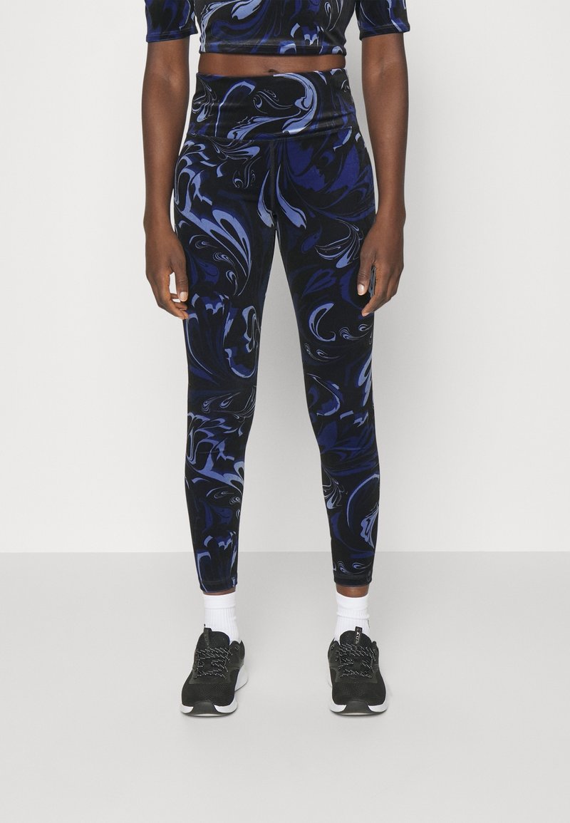 Legging noirs avec un motif de tourbillon abstrait bleu, fabriqués en matière extensible, associés à un top court assorti et des baskets noires.