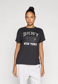 Μαύρο βαμβακερό μπλουζάκι με γκρι τυπωμένο κείμενο «DKNY 1989 NEW YORK». Κοντά μανίκια και άνετη γραμμή. Συνδυασμένο με ανοιχτό γκρι φόρμας παντελόνι.