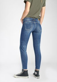 Jean en denim bleu skinny avec une taille mi-haute, présentant des poches arrière et une coupe près du corps. Associé à des baskets montantes noires.