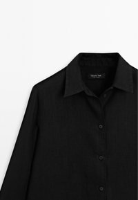 Schwarzes Hemd mit Knöpfen aus strukturiertem Stoff, mit Kragen und sieben Vorderknöpfen. Das Etikett trägt die Aufschrift "Massimo Dutti."