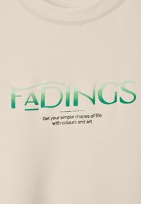 Felpa color crema con la scritta "FADINGS" in testo verde sfumato e un slogan nero sottostante. Tessuto morbido e testurizzato, design a girocollo.
