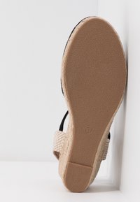 Sandale espadrille avec une tige noire, des accents en textile tissé et une semelle en jute à motifs. Taille 37 marquée sur la semelle.