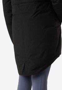 Μαύρο μονωμένο παλτό με στρογγυλεμένο κάτω μέρος, άνοιγμα στην πλάτη και ραφές, συνδυασμένο με εφαρμοστά ανοιχτό μπλε παντελόνια. Λείο ύφασμα.