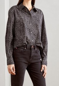 Musta nappipaita, jossa valkoisia pilkkuja, pitkät hihat ja terävä kaulus. Yhdistetty tummiin farkkuihin, joissa on korkea vyötärö ja taskut.