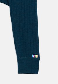 Rievota džersija ar garām piedurknēm, uz aproces ir daudzkrāsaina joslu zīme. Mīksts tekstūra un pieguļošs dizains.