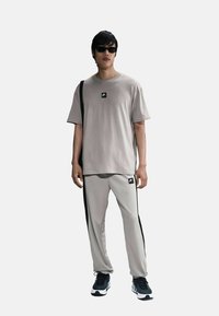Conjunto atlético de color gris claro que incluye una camiseta de manga corta y pantalones con rayas negras en los lados, complementado con gafas de sol negras y zapatos.