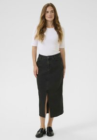 Jupe midi en denim noir avec une fente sur le devant, taille haute et coutures contrastées. Associée à un haut en coton côtelé blanc et des mocassins noirs.