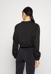 Černá zkrácená mikina s dlouhými rukávy, žebrovanými manžetami a staženým lemem. Materiál vypadá měkký a texturovaný, navržený pro přiléhavý vzhled.