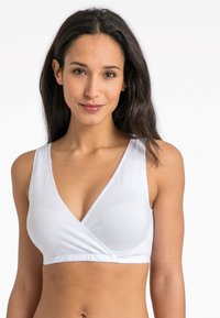 Balta apyrankė-stiliaus braletė su gilia v formos iškirpte, minkšta elastinga medžiaga ir subtilus banguotas apdaila iškirptėje ir rankogaliuose.