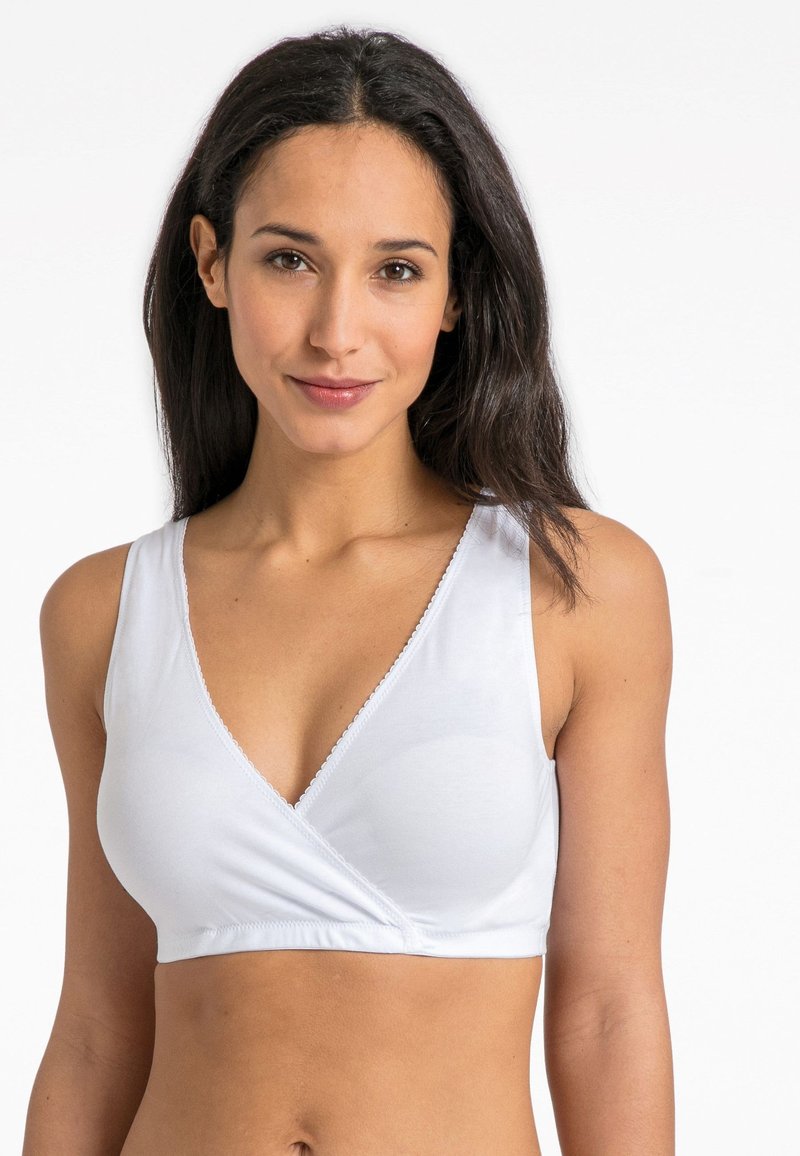 Balta apyrankė-stiliaus braletė su gilia v formos iškirpte, minkšta elastinga medžiaga ir subtilus banguotas apdaila iškirptėje ir rankogaliuose.