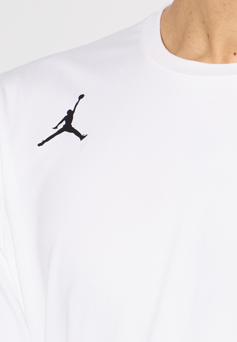 T-shirt de sport blanc avec un col rond et un logo en silhouette noire sur le côté supérieur gauche. Tissu doux, texture lisse.