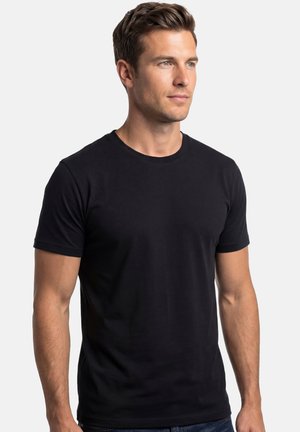 Man with short brown hair wearing a plain black short-sleeve T-shirt, looking slightly right against a white background.