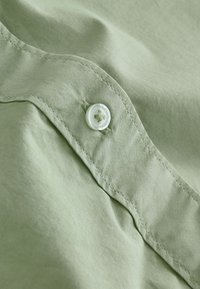 Tissu vert clair avec un bouton décoré d'un motif floral. Le tissu est lisse, avec des coutures fines et un léger éclat.